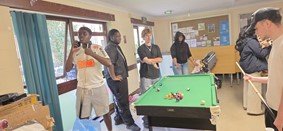 Young people and volunteers gathered around a pool table at UAA Youth Club.